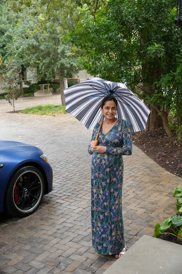 Mital beneath a striped umbrella beside an estate car