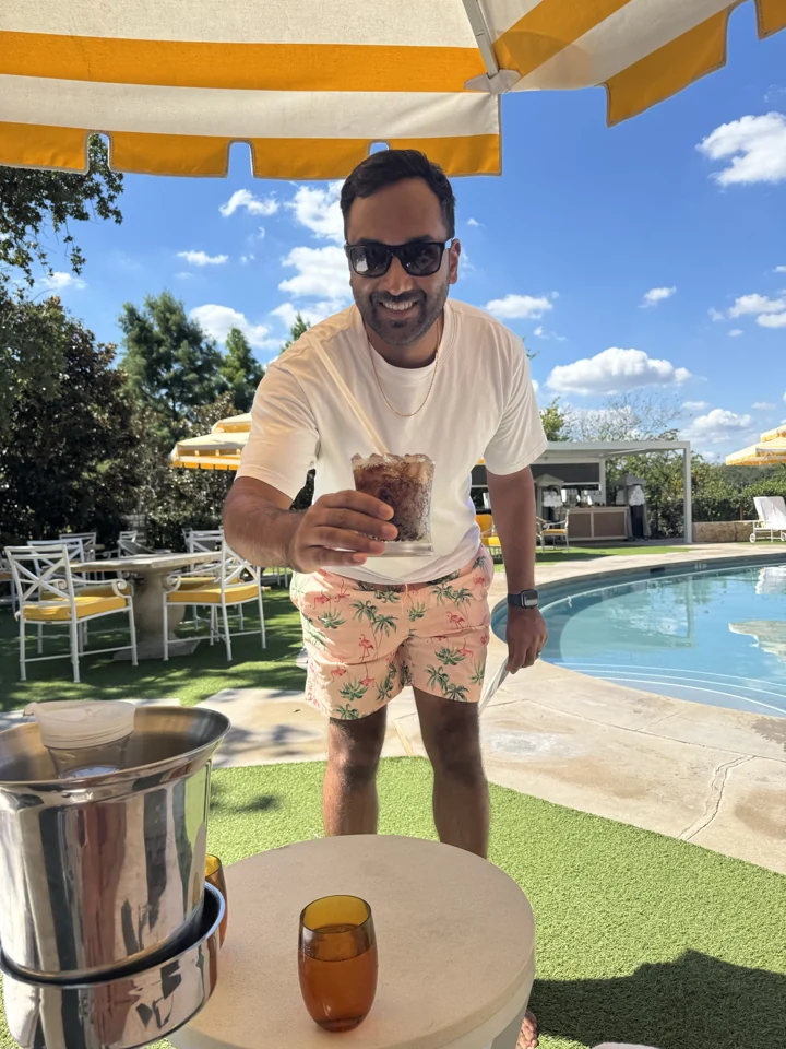 Sagar with a drink beneath the striped pool umbrella